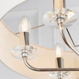 Close-up of the Castdon 6 Light Pendant in nickel, showing candle bulbs, crystal bobeche discs, and white faux silk shades against a light background.