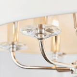 Close-up of the Castdon 6 light pendant's nickel arm and crystal bobeche detail beneath a white faux silk shade, with lit bulbs visible.