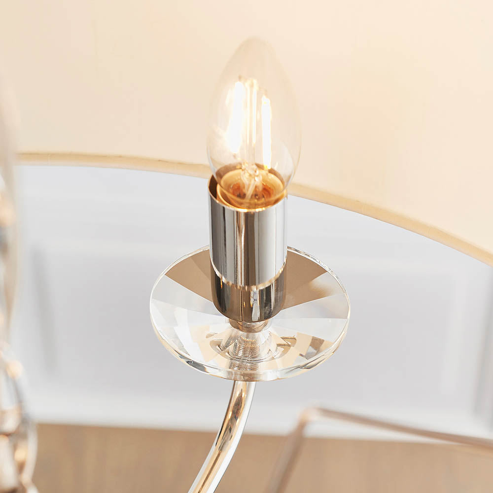 Close-up of the Castdon 6 Light Pendant's nickel arm with crystal bobeche and lit E14 candle bulb, against a cream faux silk shade.
