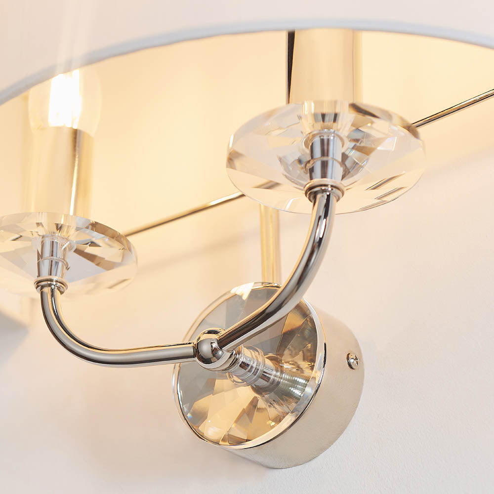 Close-up of the Castdon 2 Light Wall Light in nickel, showing curved metal arms with faceted crystal accents beneath a white fabric shade.