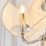 Close-up of the Castdon 2 Light Wall Light in nickel, showing a lit E14 bulb, faceted crystal disc detail and white faux silk shade.