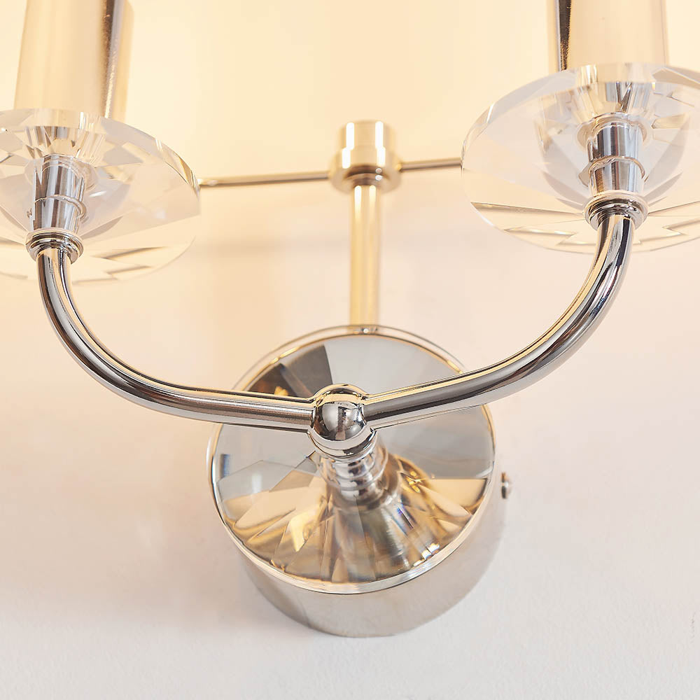 Close-up of the Castdon 2 Light Wall Light in nickel, showing curved twin arms with cut-crystal accents and E14 lamp holders.