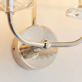 Close-up of the Castdon 2 Light Wall Light in nickel, showing curved metal arms, a crystal glass centrepiece, and wall mounting bracket detail.