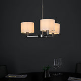 Bexley 3 Light Pendant in matt nickel with three curved arms and white faux silk drum shades, shown lit above a dark dining table.