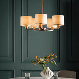 Bexley 5 Light Pendant in matt nickel with five curved arms and cream faux silk drum shades, hung above a dining table in a dark green panelled room.