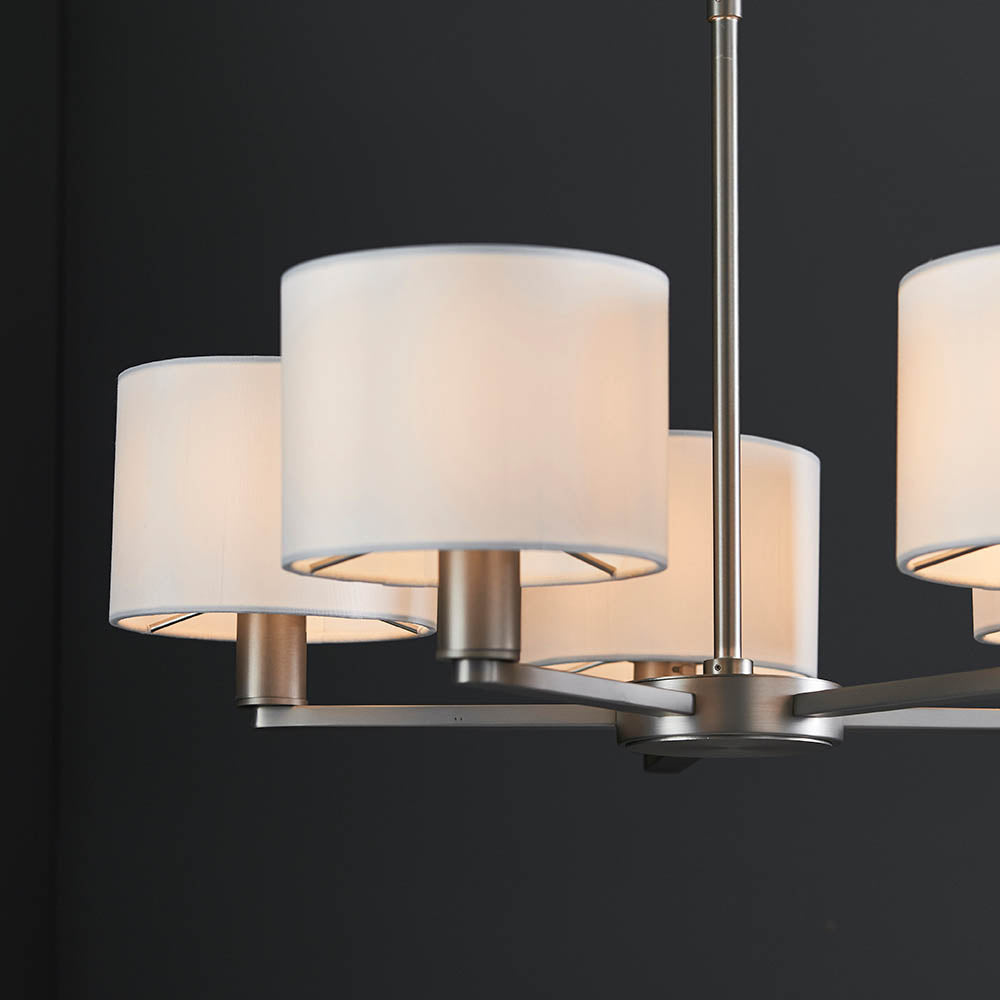 Close-up of the Bexley 5 Light Pendant in matt nickel, showing curved metal arms with white faux silk drum shades against a dark background.