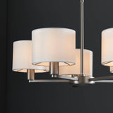 Close-up of the Bexley 5 Light Pendant in matt nickel, showing curved metal arms with white faux silk drum shades against a dark background.