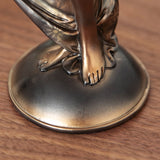 Close-up of the Lady in Draped Floral Gown resin figurine showing bare feet beneath a bronze floral-patterned gown on an oval base, set on a wooden surface.