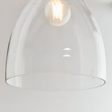 Close-up of the Endon Brackmere clear glass bell-shaped pendant shade with polished chrome trim and lit E27 filament bulb against a light background.