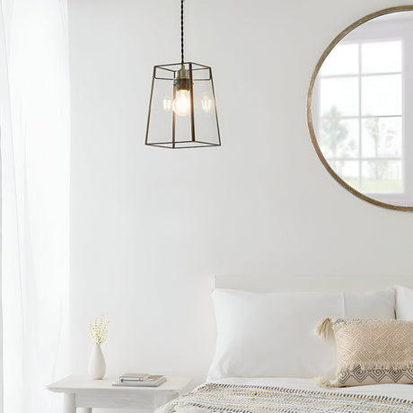 Endon Aldwell antique brass pendant light with faceted clear glass shade, hung in a bright white bedroom beside a round wood-framed mirror.