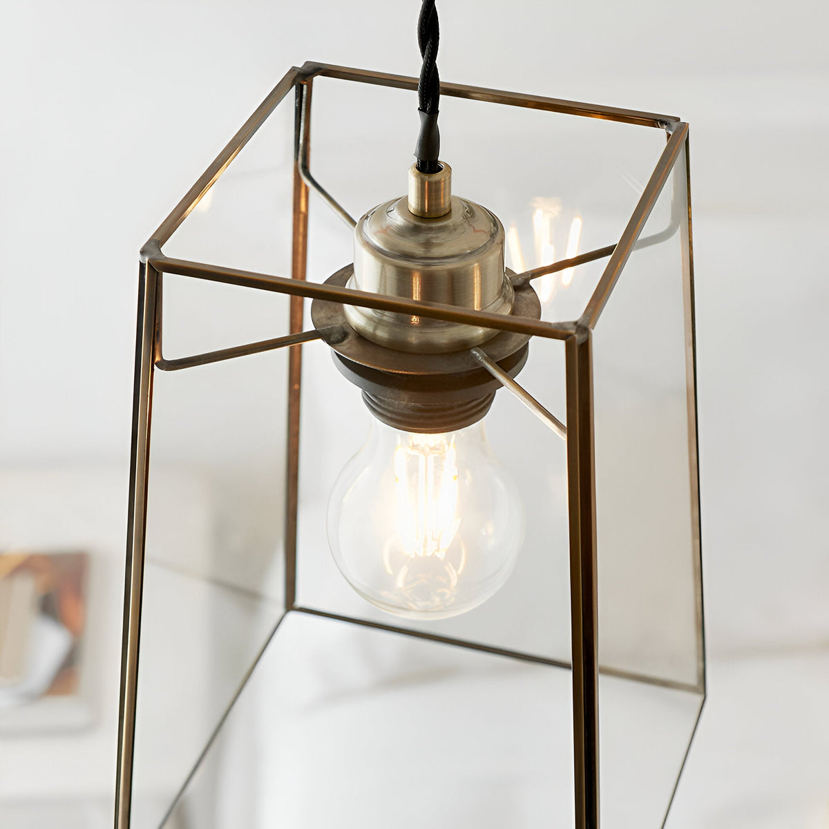 Endon Aldwell antique brass pendant light with an angular clear glass shade and filament bulb, shown lit in a bright interior setting.