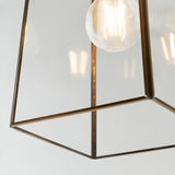 Close-up of Endon Aldwell pendant light showing the faceted clear glass shade, antique brass trim, and glowing E27 filament bulb inside.