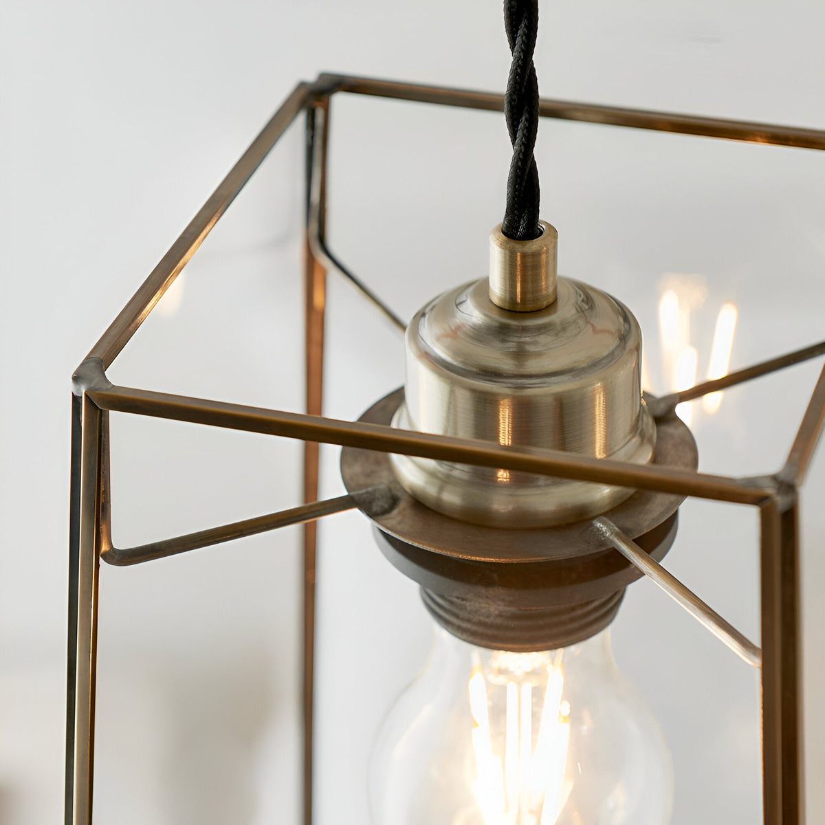 Close-up of Endon Aldwell pendant light showing antique brass lamp holder, angular glass frame, and glowing filament E27 bulb.