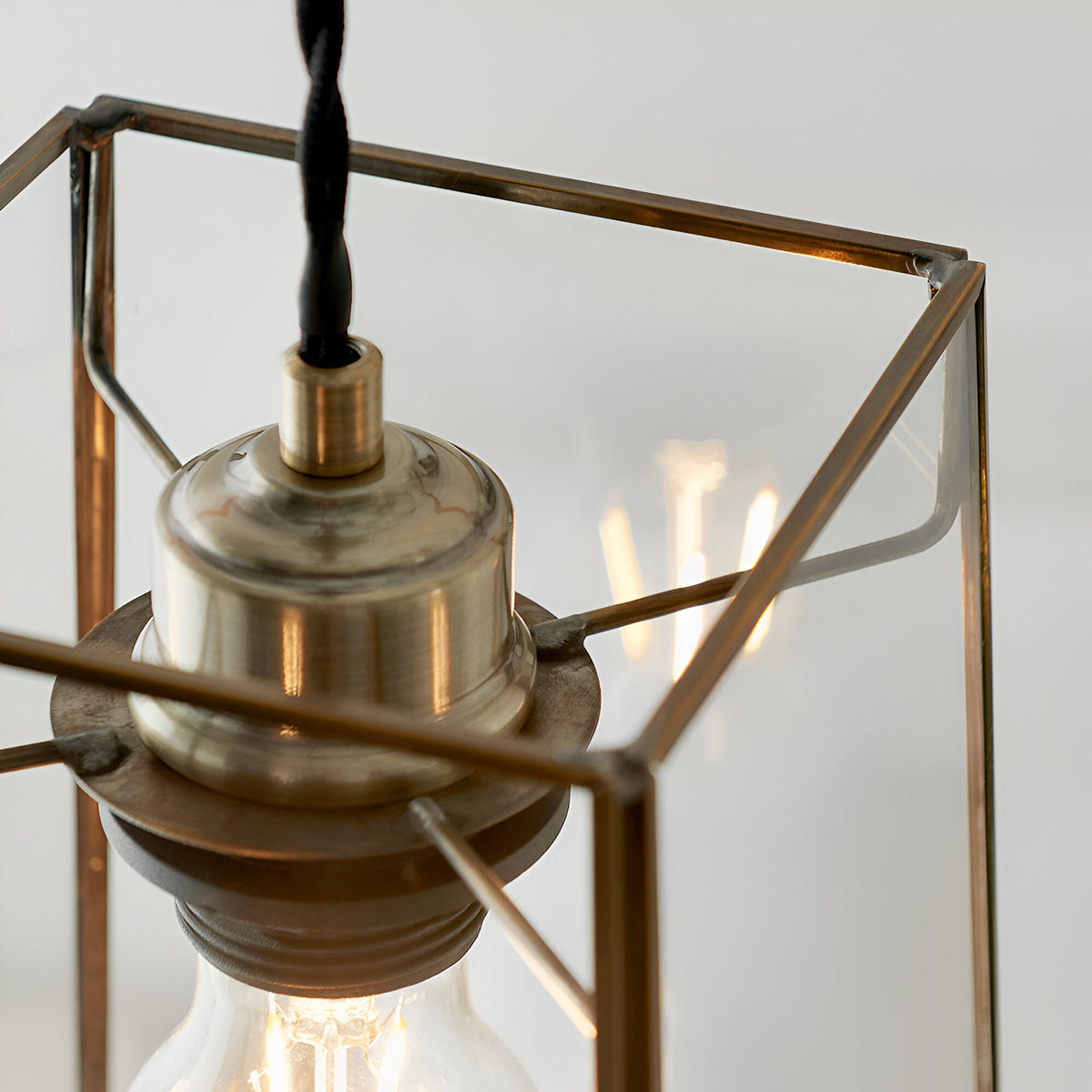 Close-up of the Endon Aldwell pendant light showing the antique brass lampholder, faceted clear glass frame and filament bulb inside.