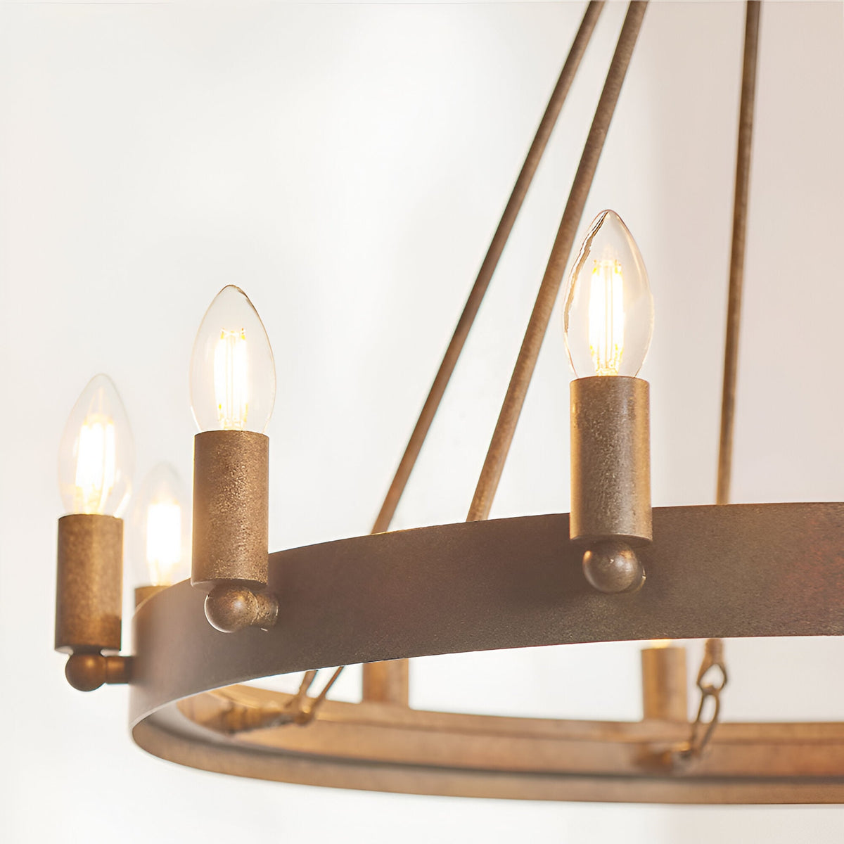 Close-up of the Bevgrove 12 Light Pendant's aged metal ring with candle-style E14 fittings and glowing filament bulbs, on a plain white background.