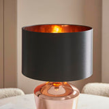 Endon Danefield table lamp with a polished copper glass base, black drum shade with copper-effect inner, and lit E27 bulb, on a marble table.