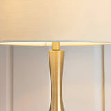 Close-up of the Endon Chartbury LED table lamp showing its slim brushed brass stem and beige fabric drum shade illuminated with warm white light.