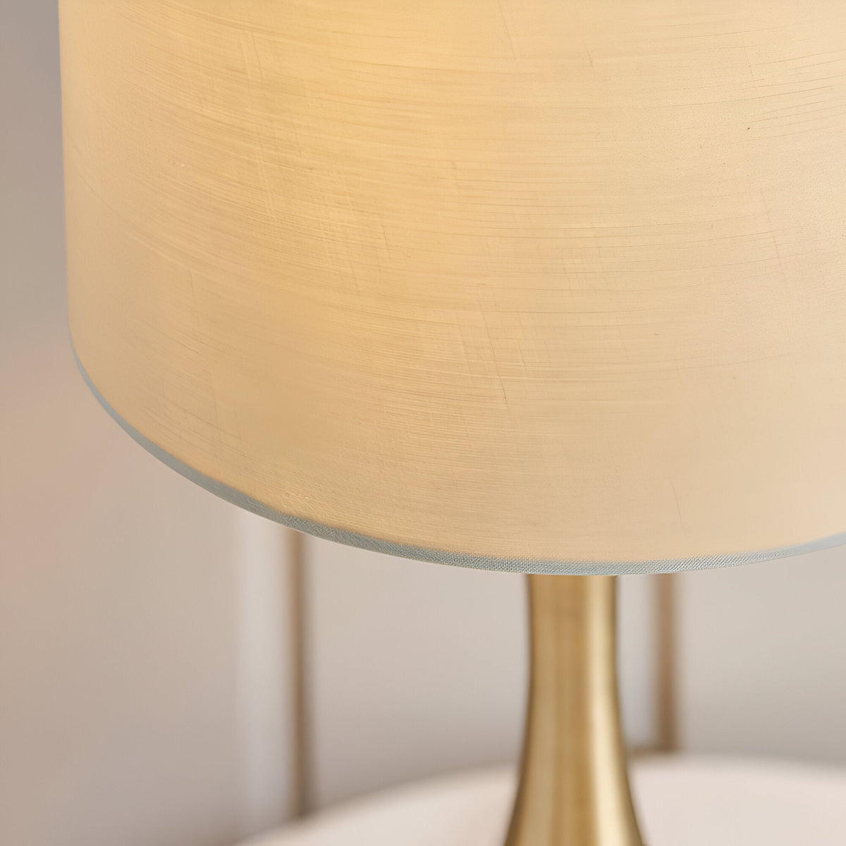 Close-up of the Endon Chartbury LED table lamp showing its brushed brass stem and beige fabric drum shade illuminated with warm white light.