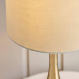 Close-up of the Endon Chartbury LED table lamp showing its brushed brass stem and beige fabric drum shade illuminated with warm white light.