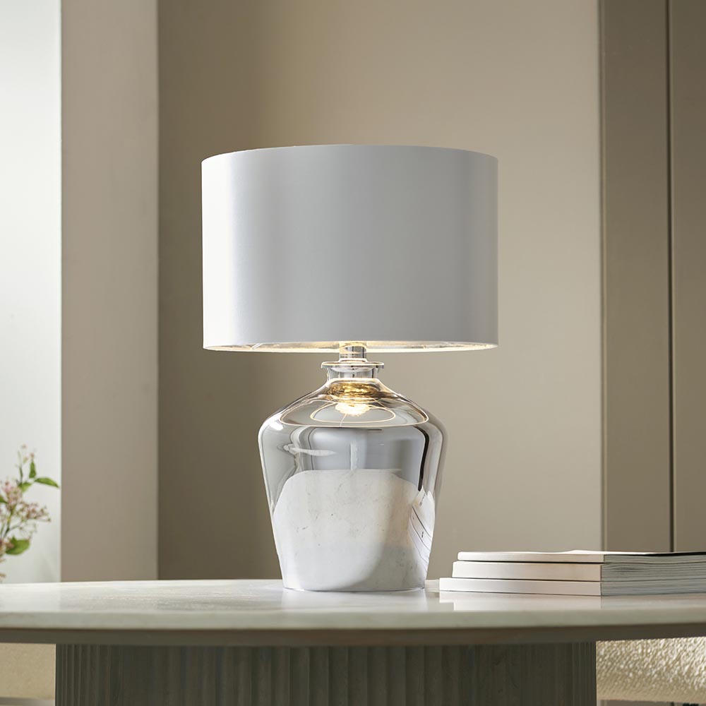 Danefield Table Lamp in chrome and cream, glass base with marbled effect, cream drum fabric shade, lit E27 bulb, shown on a table in a living room.