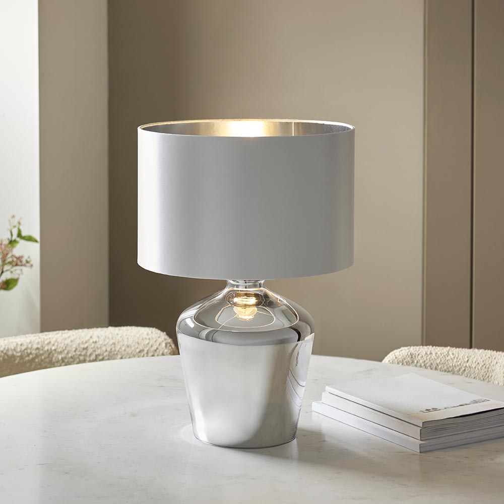 Danefield Table Lamp in chrome and cream, glass base with fabric drum shade, lit E27 bulb, shown on a marble table in a neutral room.