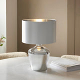 Danefield Table Lamp in chrome and cream, glass base with fabric drum shade, lit E27 bulb, shown on a marble table in a neutral room.