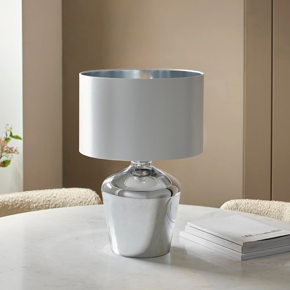Danefield Table Lamp with mirrored chrome glass base and cream fabric drum shade, styled on a marble table in a neutral living room setting.