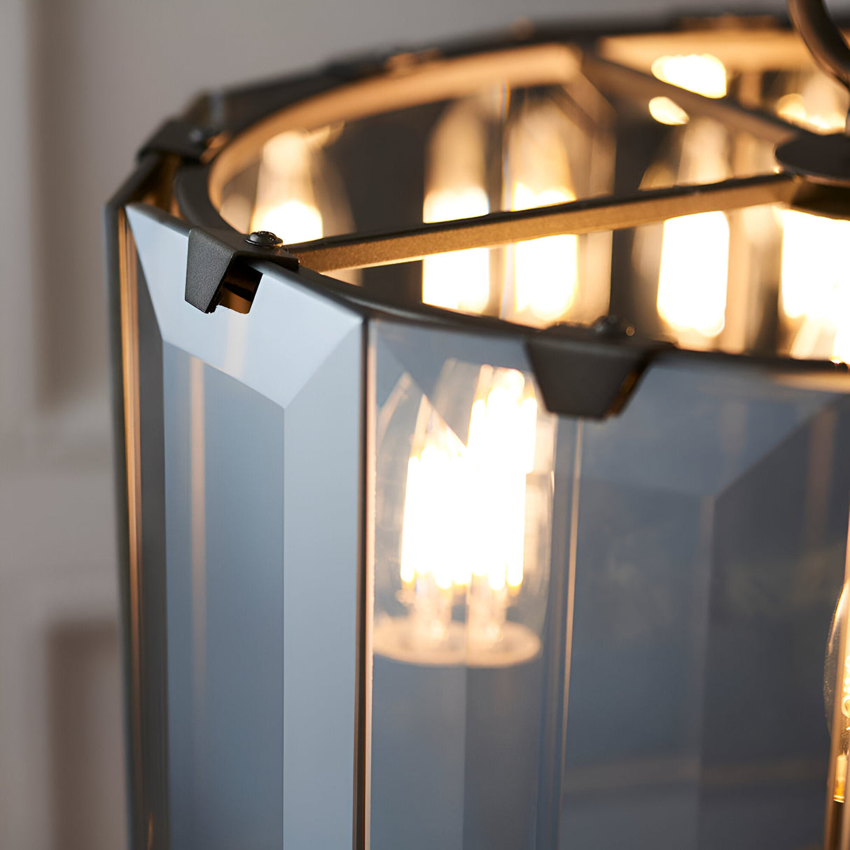 Close-up of the Bevshaw 4 Light Pendant in slate grey, showing bevelled smoke glass panels and metal frame joints around illuminated bulbs.