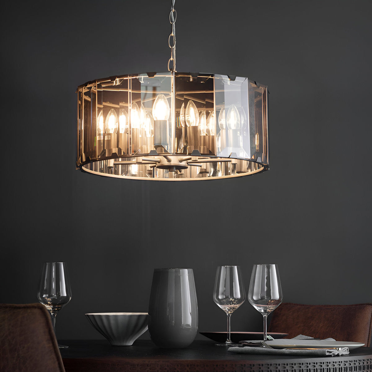 Endon Bevshaw 8 light pendant with bevelled smoke glass panels and slate grey frame, lit above a dining table set with wine glasses against a dark wall.