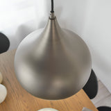 Ashleigh Pendant in matt nickel, teardrop-shaped metal shade with tapered neck, hung above a wood table in a dining setting.