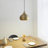 Endon Ashleigh brass pendant light with a curved teardrop shade hanging above a wooden dining table set with plates, wine glasses and a vase.