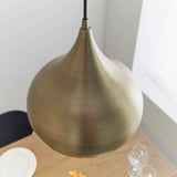 Endon Ashleigh onion-shaped pendant light in matt antique brass, hanging from a black flex above a wooden table with glassware in a bright corner.