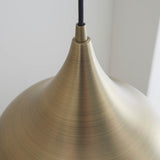 Close-up of the Endon Ashleigh pendant light showing its curved brass shade with brushed matt finish and black fabric flex against a white background.