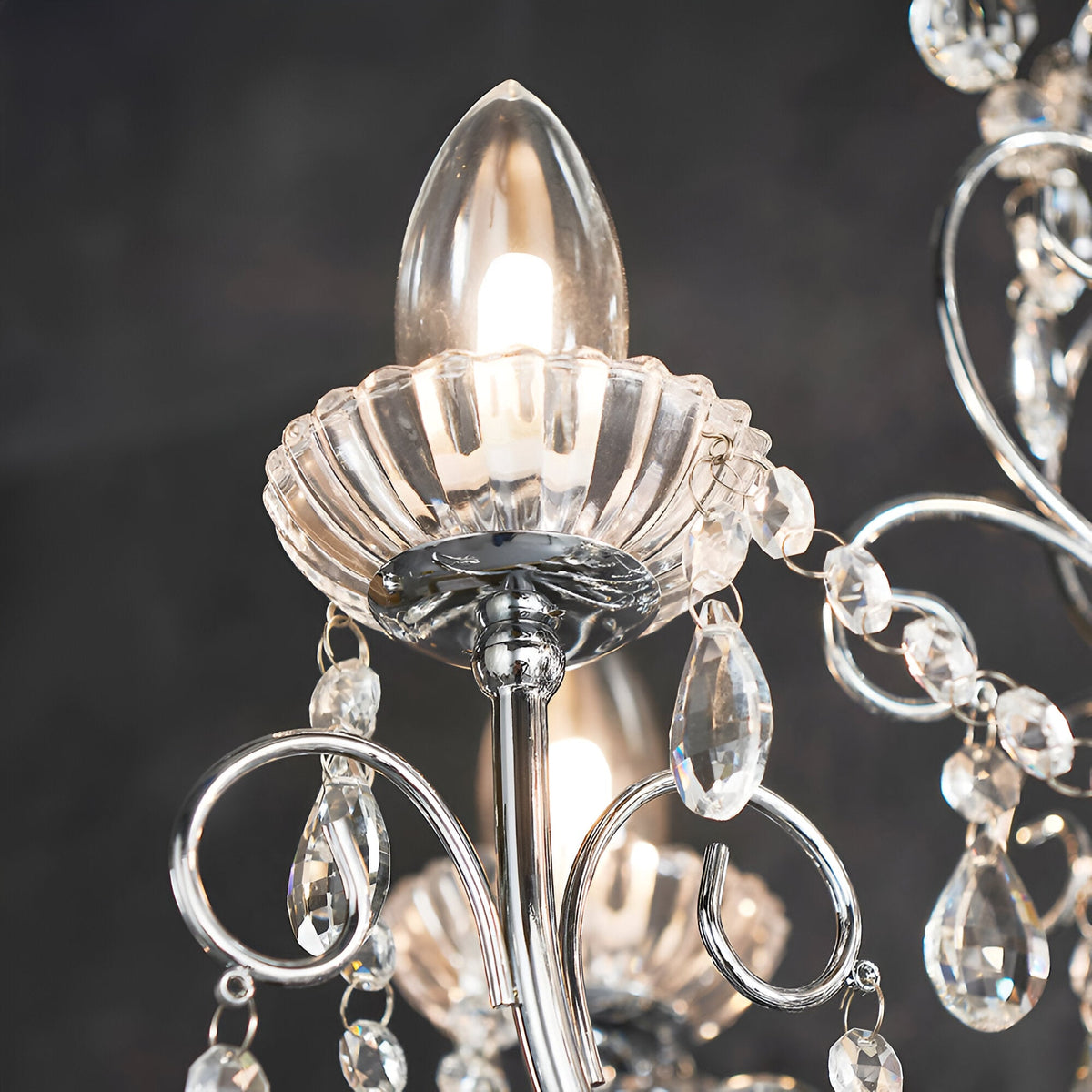 Close-up of Endon Crandon 5 light bathroom chandelier in polished chrome, showing a candle bulb, fluted glass cup, scrolled arms and clear crystal droplets.
