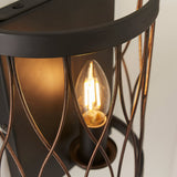 Close-up of Endon Hulton wall light in matt black and rustic bronze, showing the lit E14 candle bulb within the curved steel cage frame.