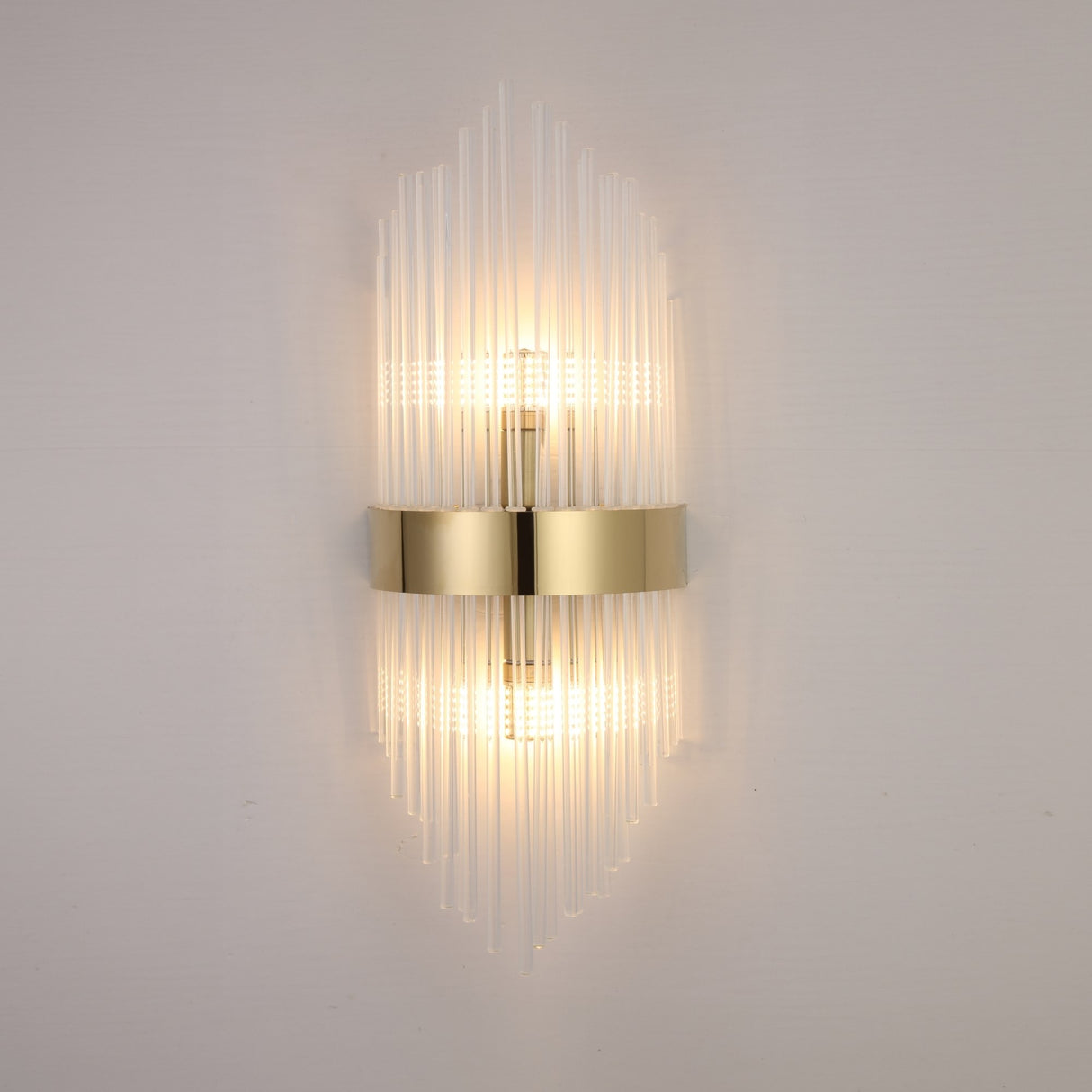 The Oriana 2 Light Crystal Wall Light - Gold features a central gold band and vertical glass rods, casting warm light up and down for a luxurious effect on any plain light wall.
