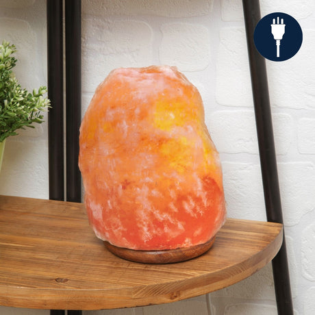 Himalayan rock salt lamp with rugged pink and orange natural stone on a round wooden base, glowing warmly on a shelf, UK plug icon shown.