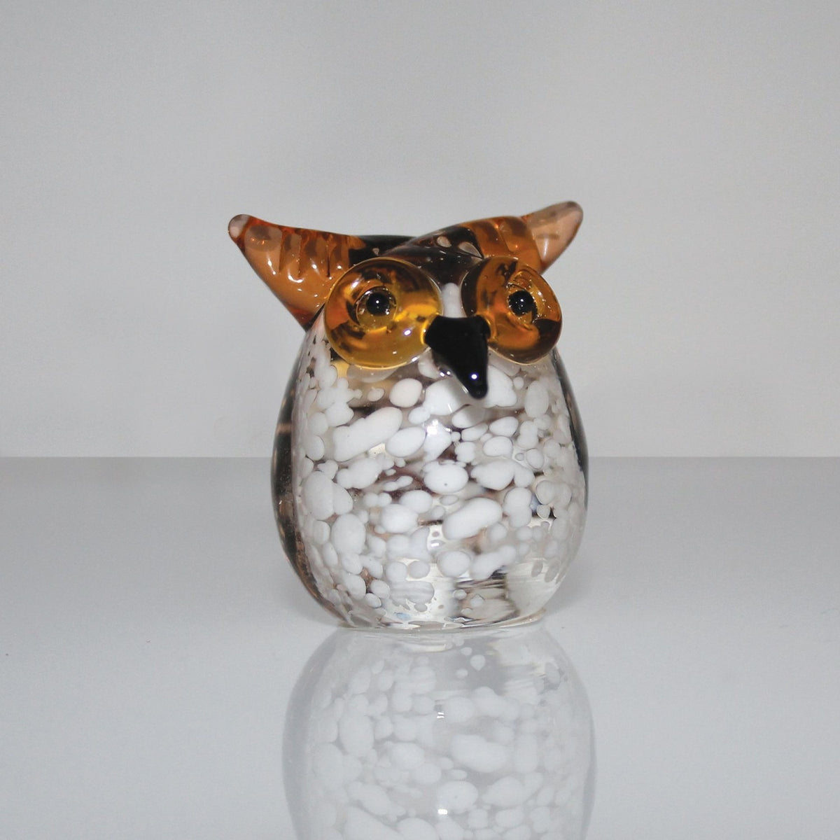 Miniature glass owl figurine with round white-speckled clear glass body, brown head, pointed ear tufts, and wide brown eyes, set against a plain light background.