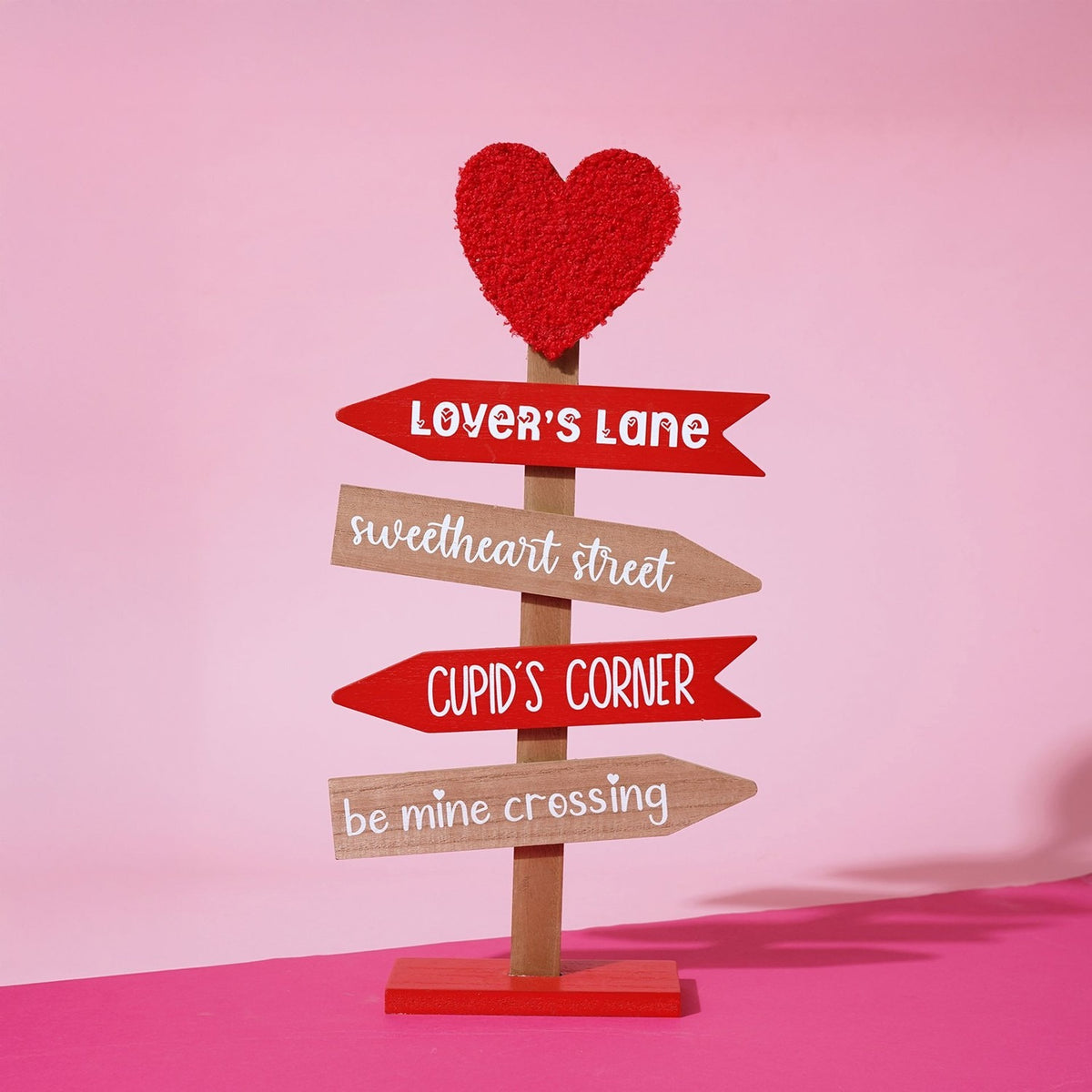 MDF Valentine's signpost wall art with a red fabric heart topper and four arrows reading Lover's Lane, Sweetheart Street, Cupid's Corner and Be Mine Crossing.