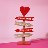 MDF Valentine's signpost wall art with a red fabric heart topper and four arrows reading Lover's Lane, Sweetheart Street, Cupid's Corner and Be Mine Crossing.