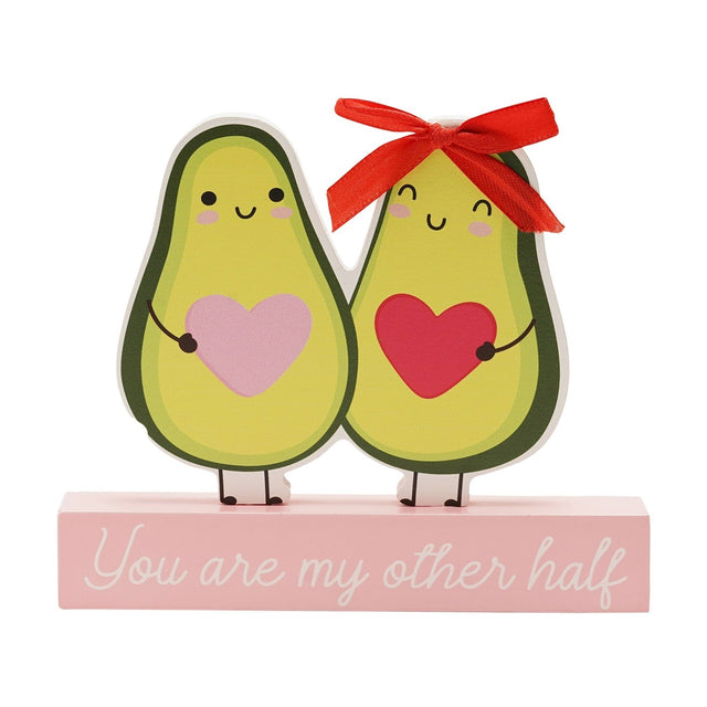 Wooden plaque featuring two smiling avocado figures holding pink and red hearts, one with a red ribbon bow, on a pale pink base reading "You are my other half", set against a plain white background.