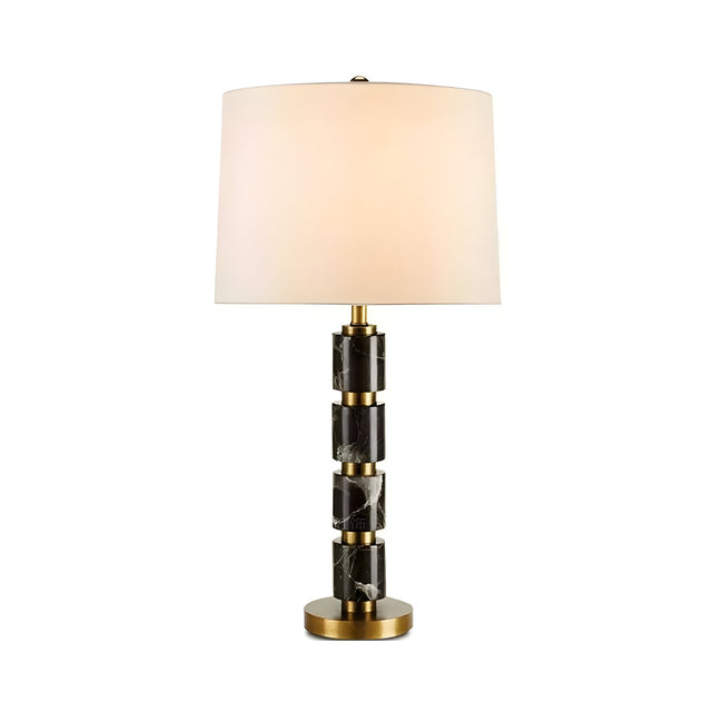 The Noirion 1 Light Stacked Marble Table Lamp features a sculptural brass and black cylindrical base with stacked marble and gold sections, topped with a modern white drum-shaped shade and finished with a round brass bottom.
