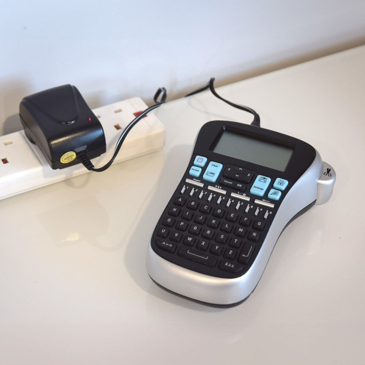 Mercury SMDC401UK 12W switch-mode power supply by AVSL plugged into a white UK extension lead beside a label maker on a light worktop.