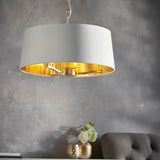 Endon Brendale 3 light pendant with a white faux silk drum shade and metallic gold inner lining, hanging above a console with roses in a living room.