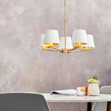 Brendale 5 Light Pendant in satin gold, with white faux silk shades and gold inner linings, hung above a dining table in a soft grey room.