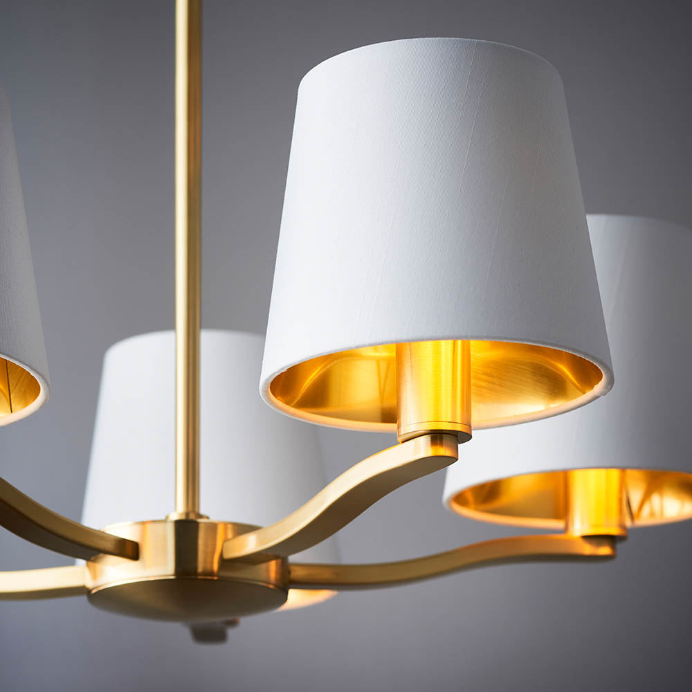 Brendale 5 Light Pendant in satin gold, close-up of white faux silk shades with gold inner lining on curved brushed gold arms, grey background.