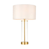 Endon Caldley table lamp with clear cylindrical glass base, satin brass fittings and vintage white faux silk drum shade, on a plain white background.