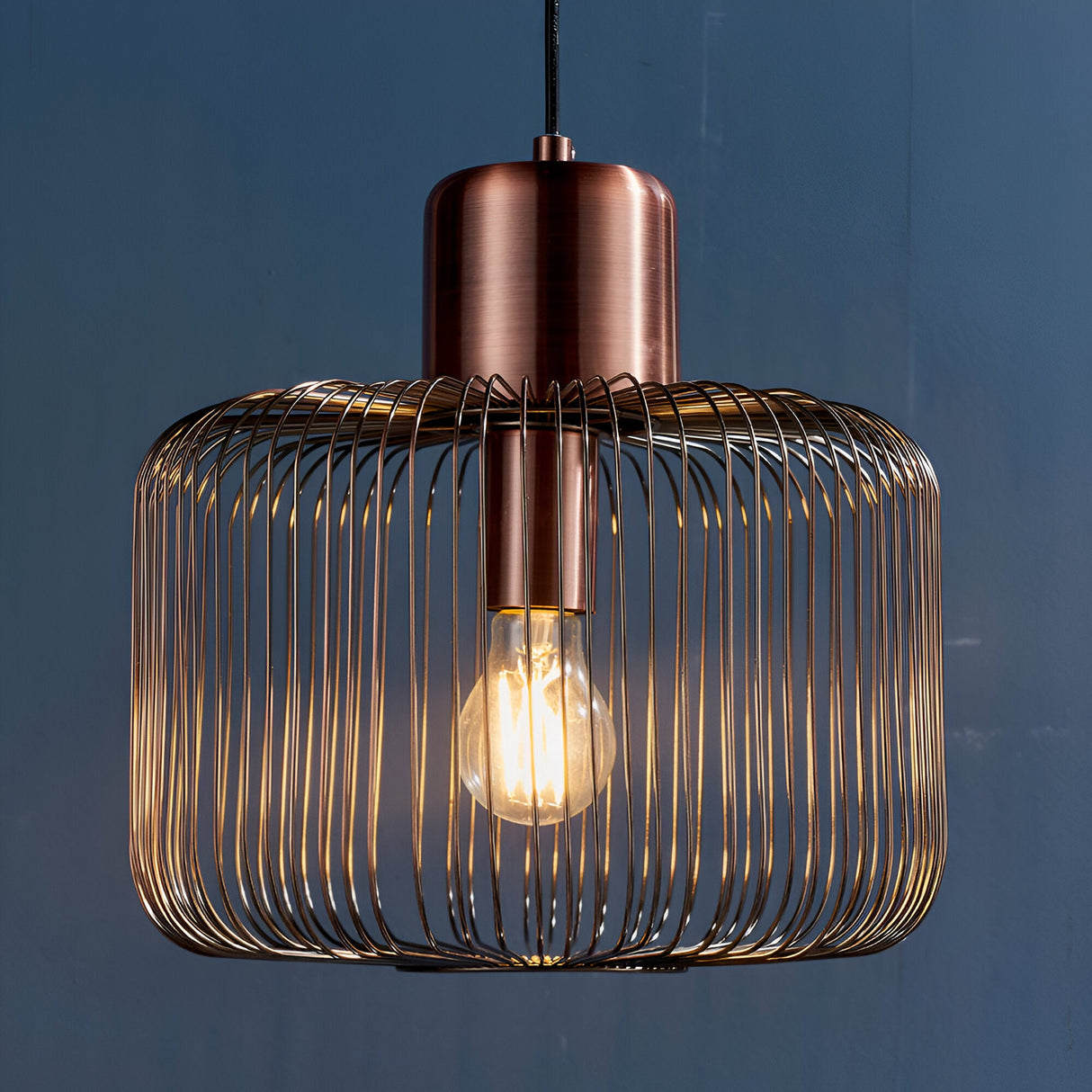 Castdale Cage Pendant in antique copper with a single-light open wire cage shade, visible bulb, and cylindrical metal fitting on black flex.