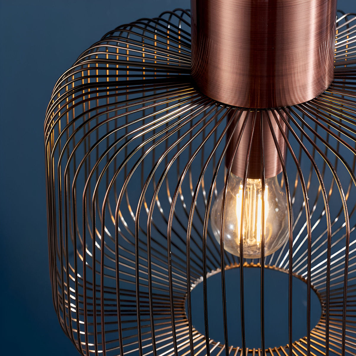 Close-up of the Castdale Cage Pendant in antique copper, showing the open wire cage shade and exposed E27 bulb against a dark blue background.