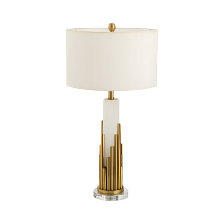 The Celora 1 Light Vertical Spire Alabaster Table Lamp in Brass & Soft White adds sculptural design to any space with its white cylindrical shade, geometric base featuring vertical gold rods, and round clear acrylic bottom.